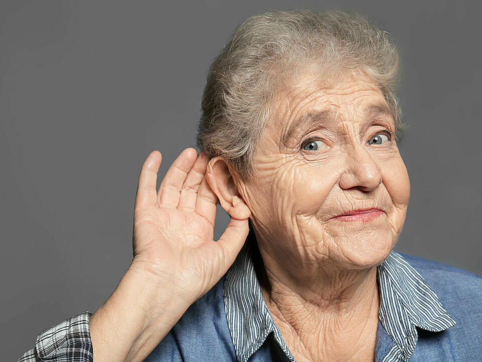 Elderly woman with hearing problem on grey background